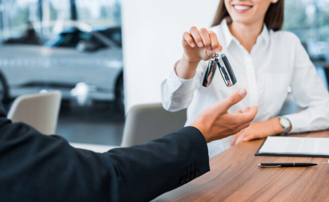 cropped view of happy car dealer giving car key to man